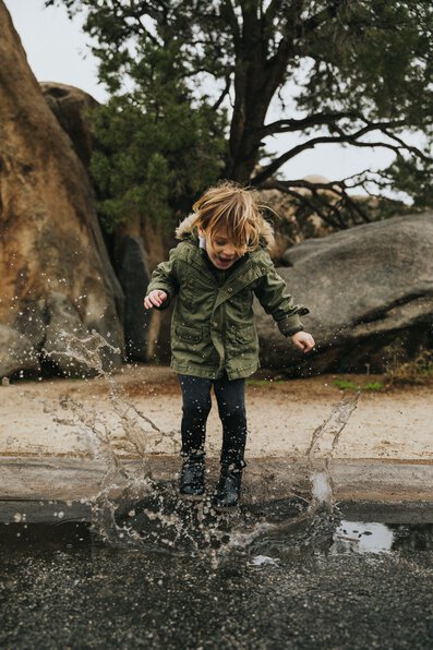 kid jumping in puddle in jacket
